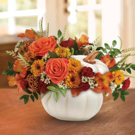 Orange and red floral arrangement in a white pumpkin vase
