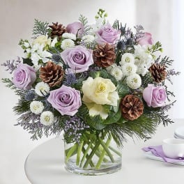 Lavender and white roses arranged in a clear glass vase with pinecones