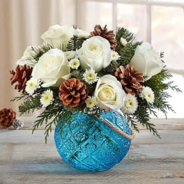 White roses and pinecones arranged in a blue glass vase