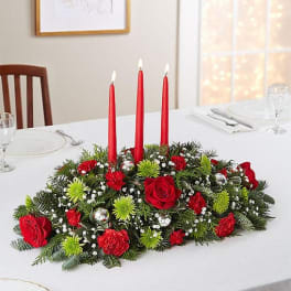 Red floral centerpiece with three tall red candles on a dining table