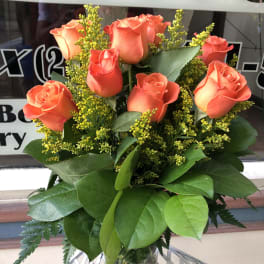 Orange roses in a clear glass vase with yellow filler flowers