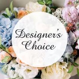 Assorted pastel flowers arranged around a round sign reading "Designer's Choice"