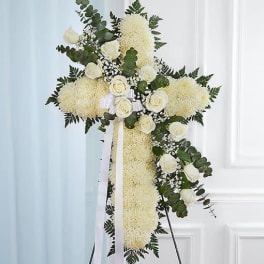 White floral standing cross with roses and greenery on an easel