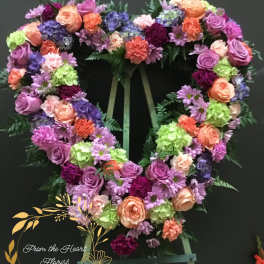 Heart-shaped floral wreath on an easel with pink, purple, peach, and green blooms