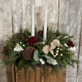 Holiday centerpiece with white candles, red flowers, and greenery in a wooden box