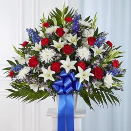 Large standing floral spray with red roses, white lilies, and blue accents