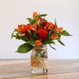 Red roses and orange alstroemeria in a mason jar vase