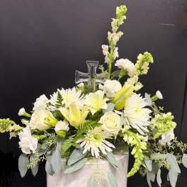 White floral arrangement with a clear cross pick in a pale container
