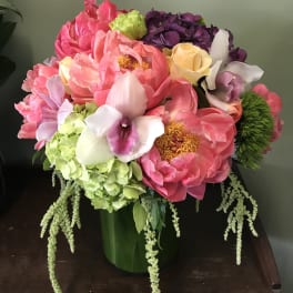 Colorful bouquet of pink peonies, hydrangeas, orchids, and roses in a green vase