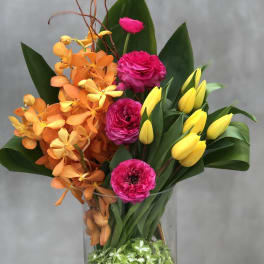 Bright orange and pink flowers with yellow tulips in a glass vase