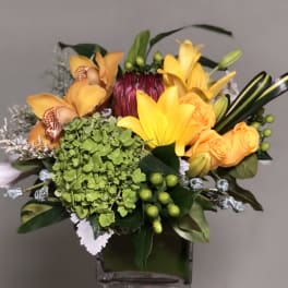 Bouquet of yellow lilies, orange roses, and green hydrangea in a glass vase