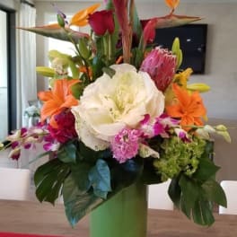 Tropical flower arrangement in a green vase with orange and pink blooms