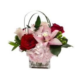 Short arrangement of pink hydrangea with red roses and a pink orchid in a glass cube vase