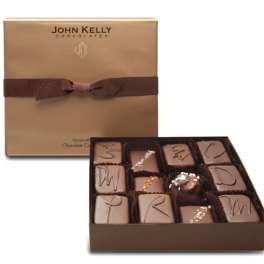 Square gold gift box with brown ribbon and assorted gourmet chocolates in an open tray.