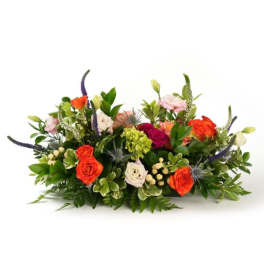 Low centerpiece of bright orange and pink roses with mixed blooms and berries in a horizontal arrangement