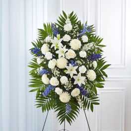 Standing spray of white lilies, roses, and mums with blue flowers on an easel