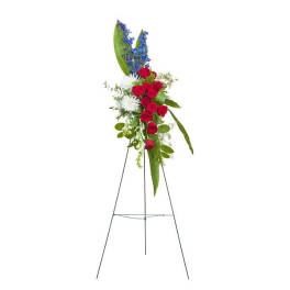 Standing red, white, and blue floral spray with roses, mums, and delphinium on a metal easel.