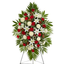 Standing spray of red roses, white lilies, and white mums with large palm fronds on an easel