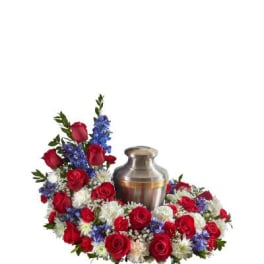 Cremation urn surrounded by red, white, and blue flowers in a circular sympathy arrangement
