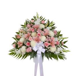 Fan-shaped standing arrangement of pink lilies, roses, and white mums with a white bow.