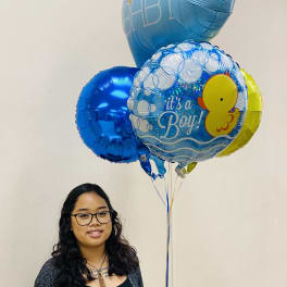 Person holding a bundle of blue baby boy themed balloons with duck and hello baby text