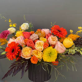 Bright mixed bouquet in a dark vase with roses, gerberas, and yellow blooms