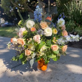 Mixed bouquet of pastel flowers in a clear vase filled with oranges