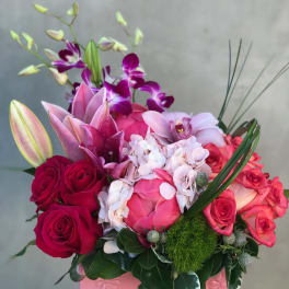 Pink and red floral arrangement in a pink box with roses, orchids, and lilies