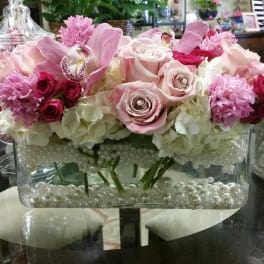 Pink and white floral arrangement in a clear rectangular vase with pearl accents