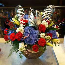 Red roses and blue hydrangeas in a bronze bowl with patriotic ribbon curls