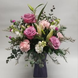 Pink roses and lilies in a purple vase with greenery