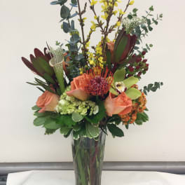 Tall mixed bouquet in a clear glass vase with peach roses and yellow blooms