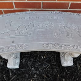 Stone sign reading welcome to the farm with a tractor and barn design
