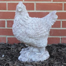 White chicken statue on mulch in front of a brick wall