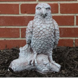Stone eagle statue on a log in front of a brick wall