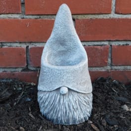 Small gray garden gnome statue against a brick wall