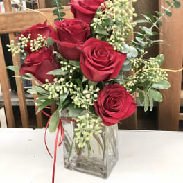 Red roses arranged in a clear square vase with greenery