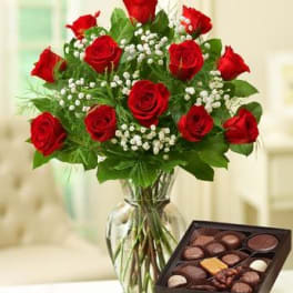 Red roses in a glass vase beside a box of chocolates