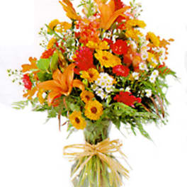 Bright orange and yellow mixed bouquet in a glass vase with a ribbon