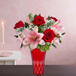 Red roses and pink lilies arranged in a red glass vase