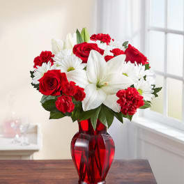 Red roses, white lilies, and daisies in a red glass vase