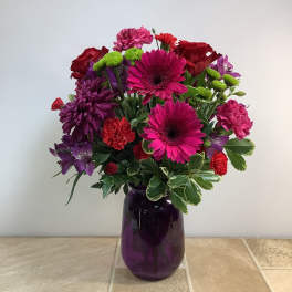 Mixed bouquet of pink, red, and purple flowers in a purple glass vase