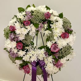 Round floral wreath with white daisies, pink roses, and a purple ribbon