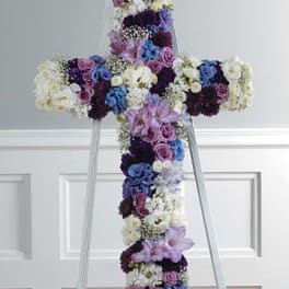 Floral cross arrangement on a standing easel with purple, blue, and white blooms