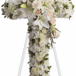 White floral cross on an easel with roses and lilies