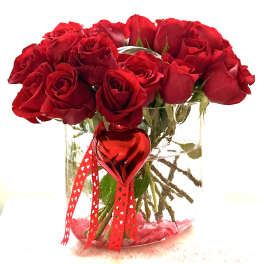 Red roses in a clear glass vase with a red heart ornament and ribbon