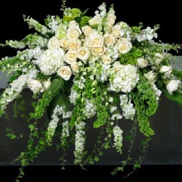 White rose and hydrangea arrangement with trailing greenery on a dark pedestal