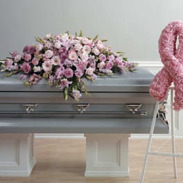 Pink floral casket spray on a gray casket beside a pink ribbon wreath
