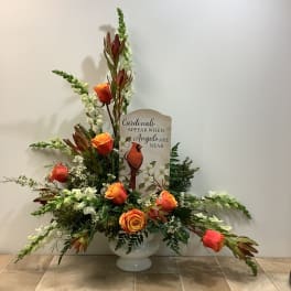 Orange roses and white flowers in a white vase with a cardinal memorial sign