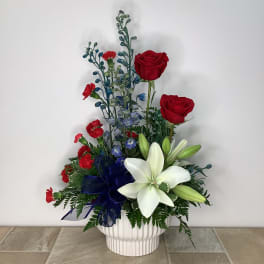 Red roses and white lilies in a white vase with a blue ribbon